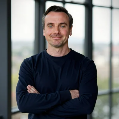 Lee Parnell smiling, standing indoors with crossed arms.